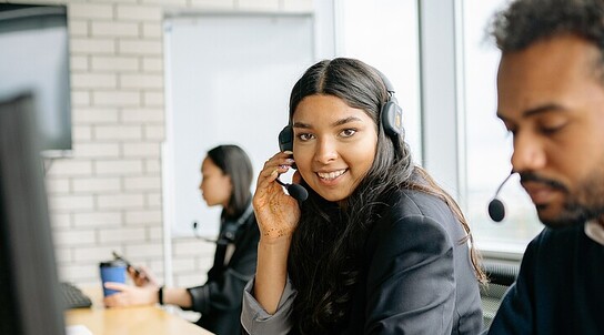 zwei junge Menschen sitzen am PC und tragen ein Headset