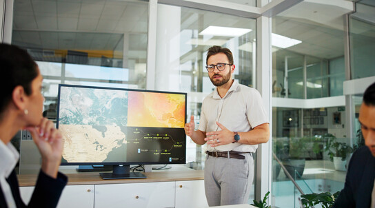 Businessman, screen or meeting with discussion for climate change, renewable energy or development at office. Man, employee or speaker with geographic data or technology display for global project