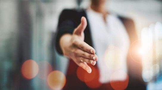Frau im Anzug reicht dem Zuschauer die Hand